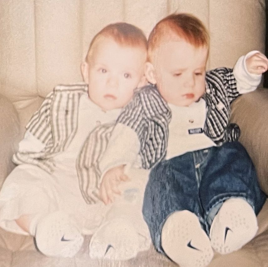 Both boys around six months old sitting up in a chair.